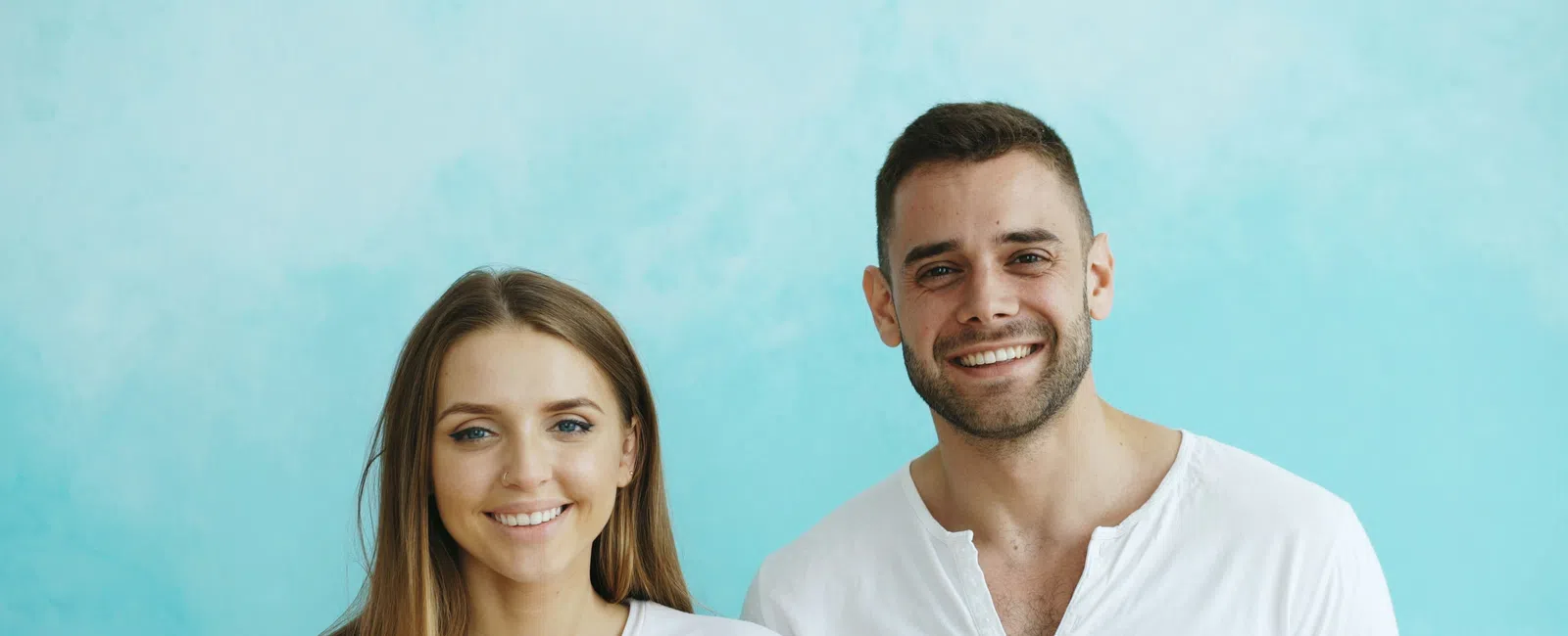 Smiling young man and woman wearing white shirts standing against a light blue background.