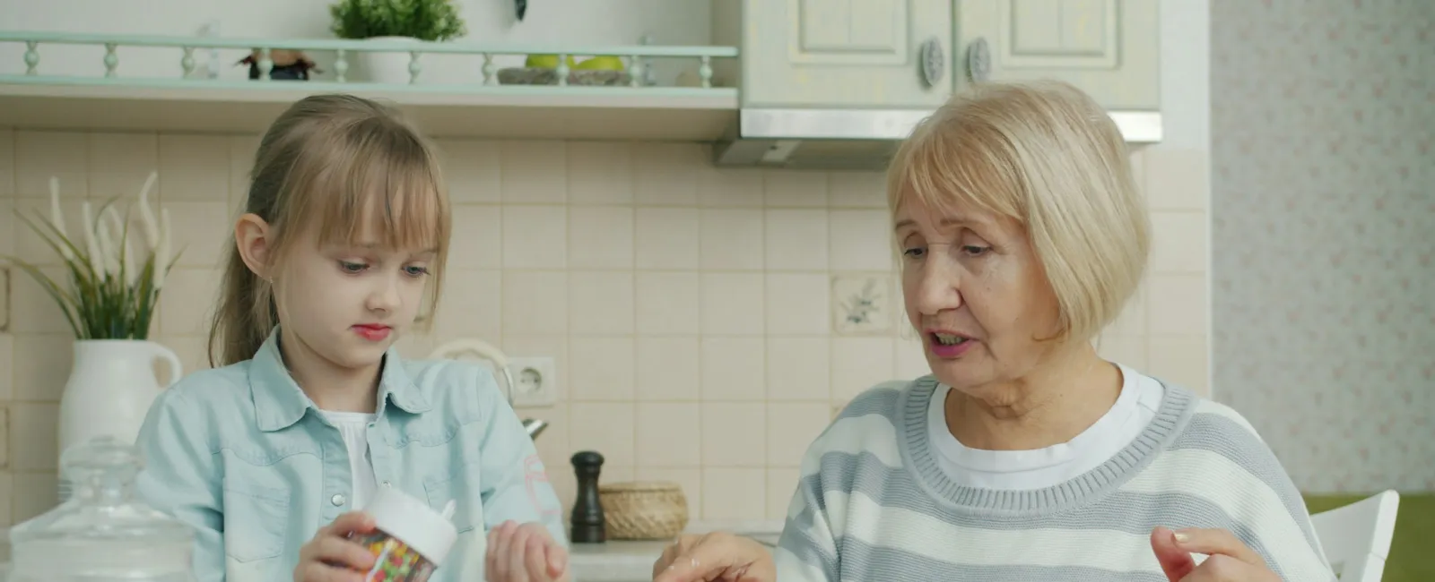 Grandmother and granddaughter decorating cupcakes together in a bright kitchen with baking ingredients on the table