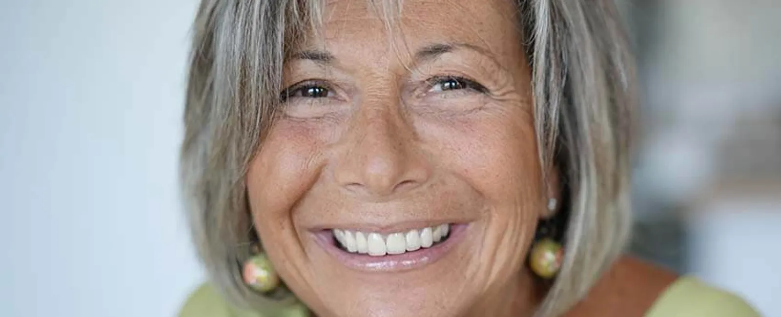 Smiling older woman with silver hair in a green top, showcasing joy and confidence indoors.