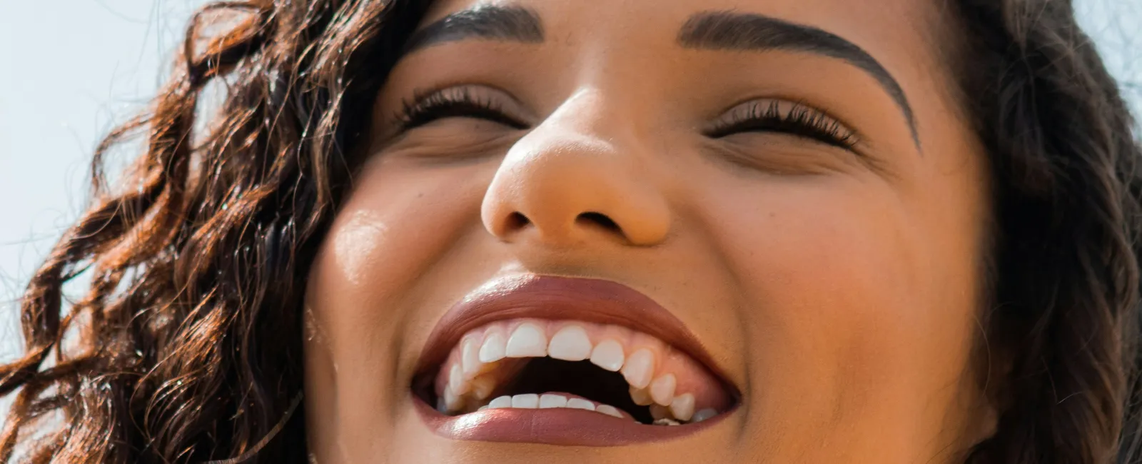 Smiling woman with curly hair enjoying a sunny day, radiating joy and positivity.