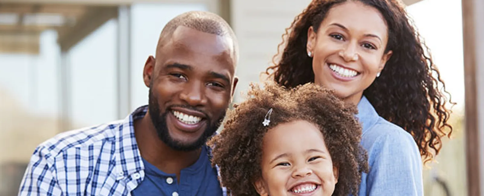 Happy family of three smiling outdoors with natural light, embracing and enjoying quality time together.
