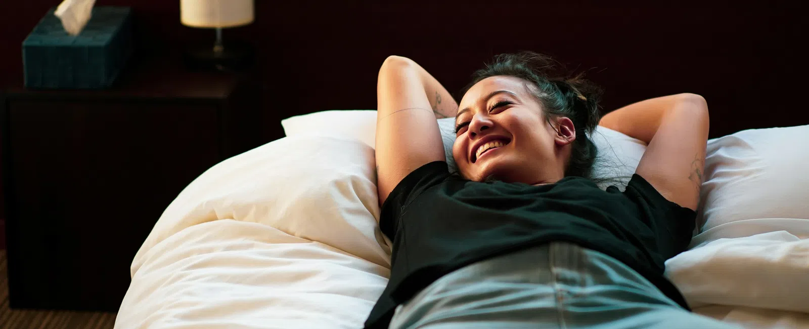 Young woman smiling and relaxing on a bed with white sheets in a cozy room.
