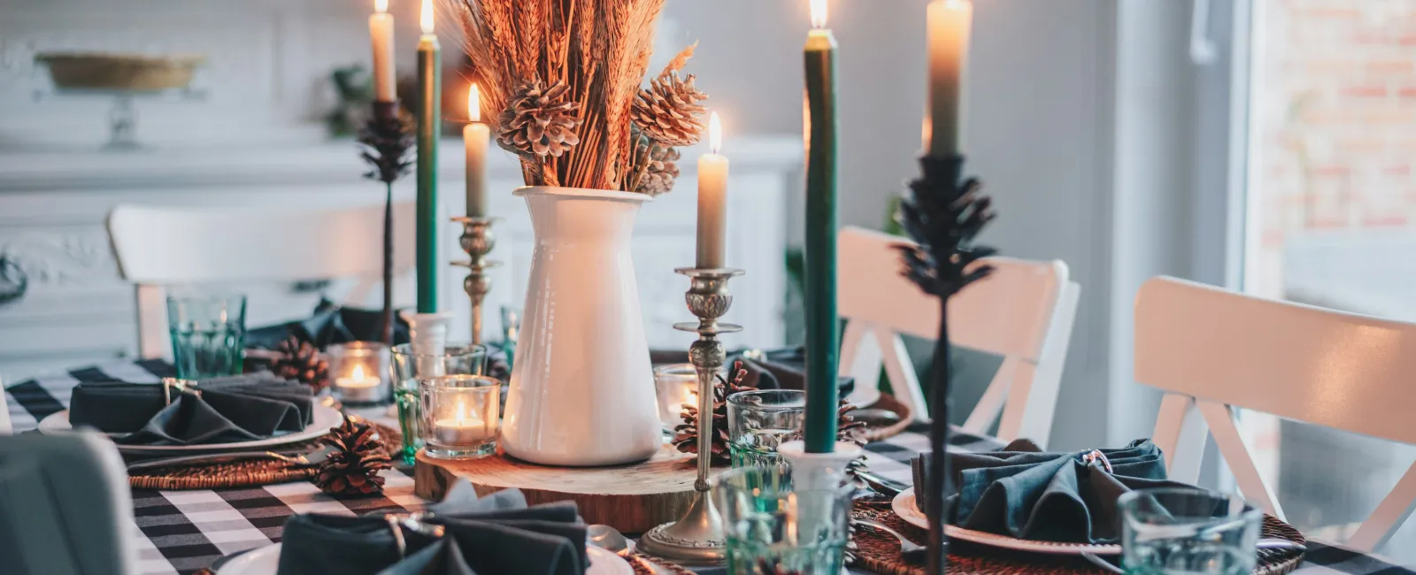 Cozy autumn dining table with black and white checkered cloth, candles, wheat centerpiece, and rustic tableware.