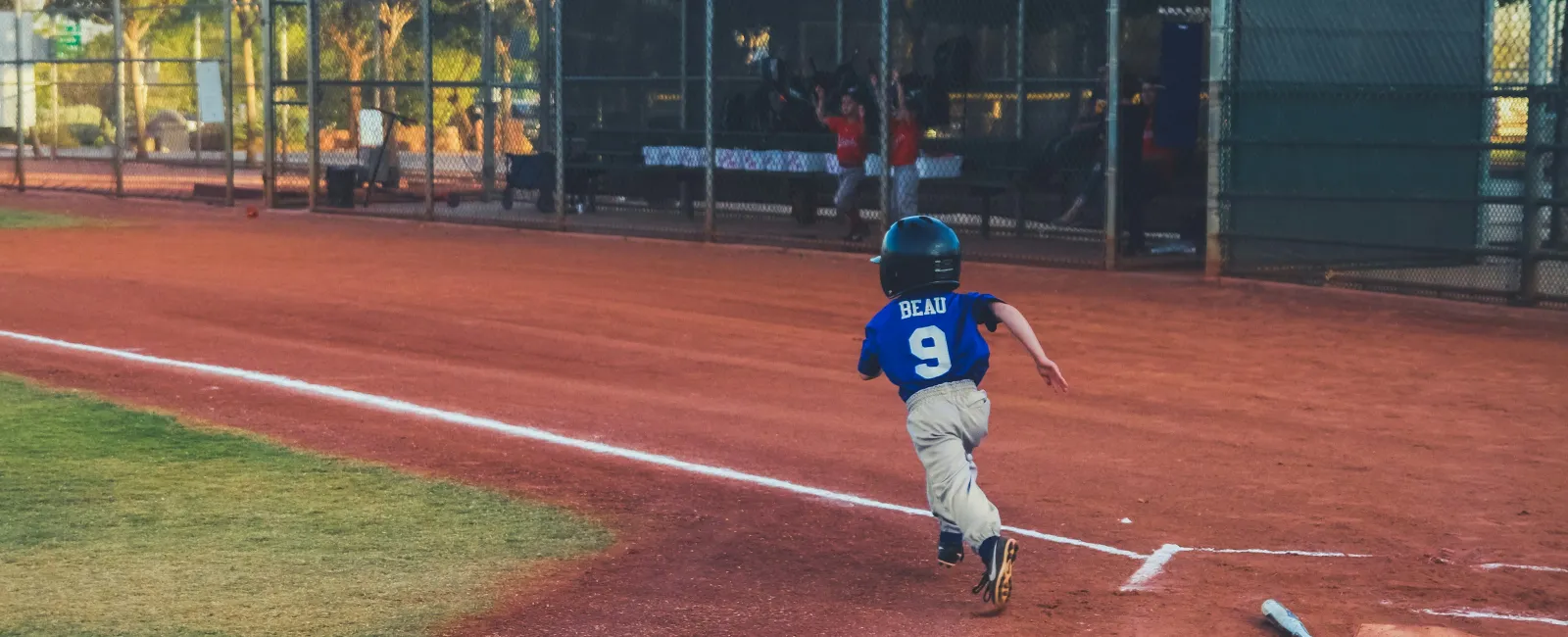 Young baseball player in blue jersey running from home plate toward first base on a sunny day