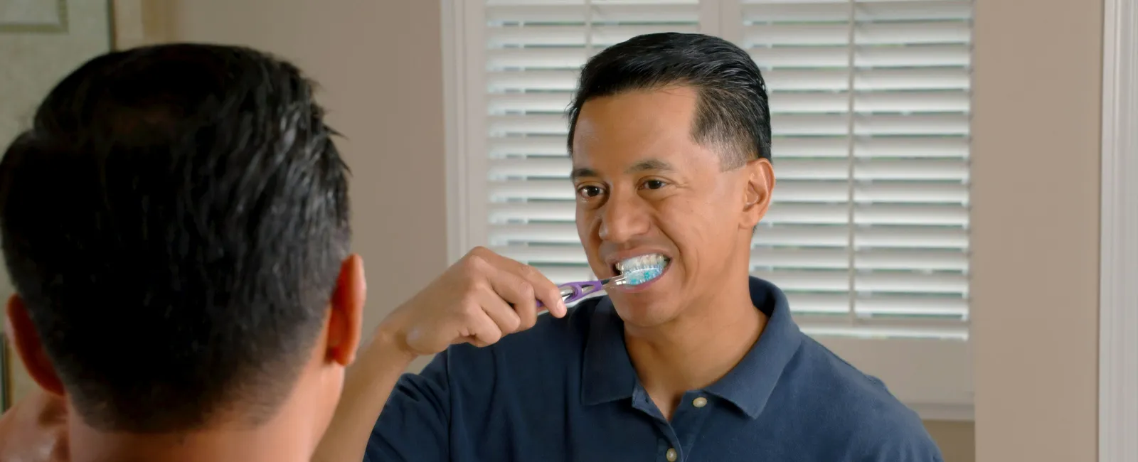 Man brushing teeth in bathroom mirror, promoting oral hygiene and daily dental care routine.