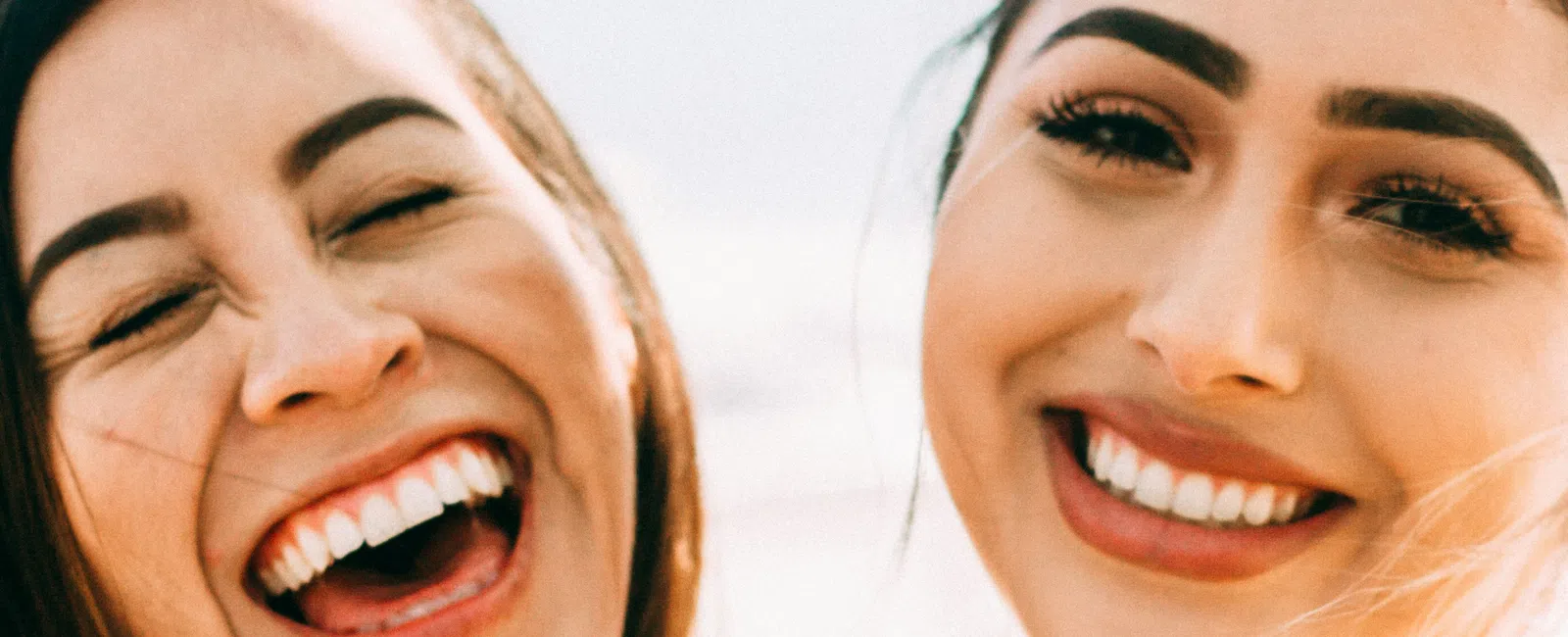 Two young women smiling and laughing outdoors enjoying a sunny day together close-up portrait.