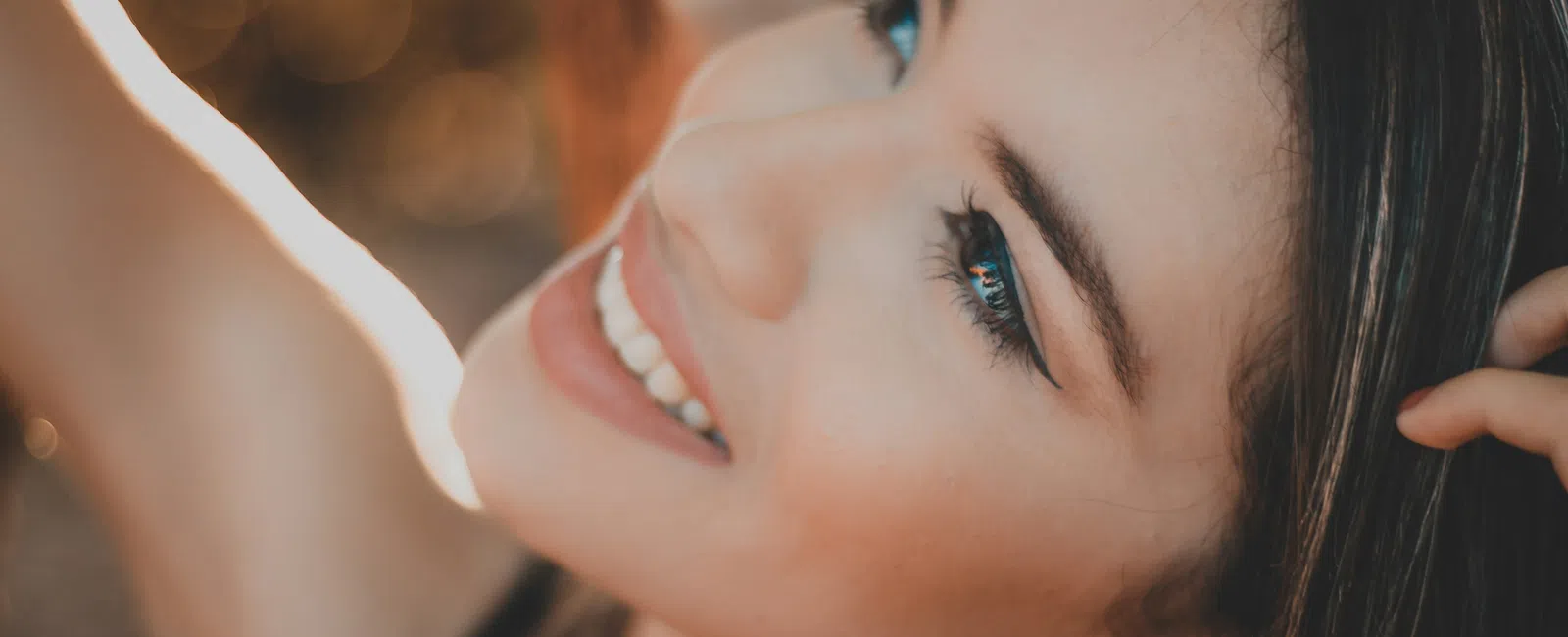Close-up of a smiling woman with long hair looking upwards in warm natural light.