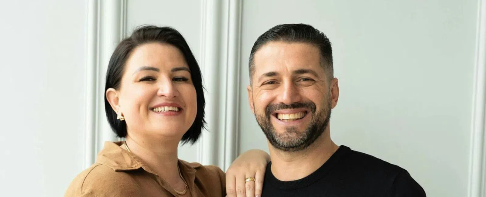 Smiling couple posing together indoors with woman in brown shirt and man in black sweater