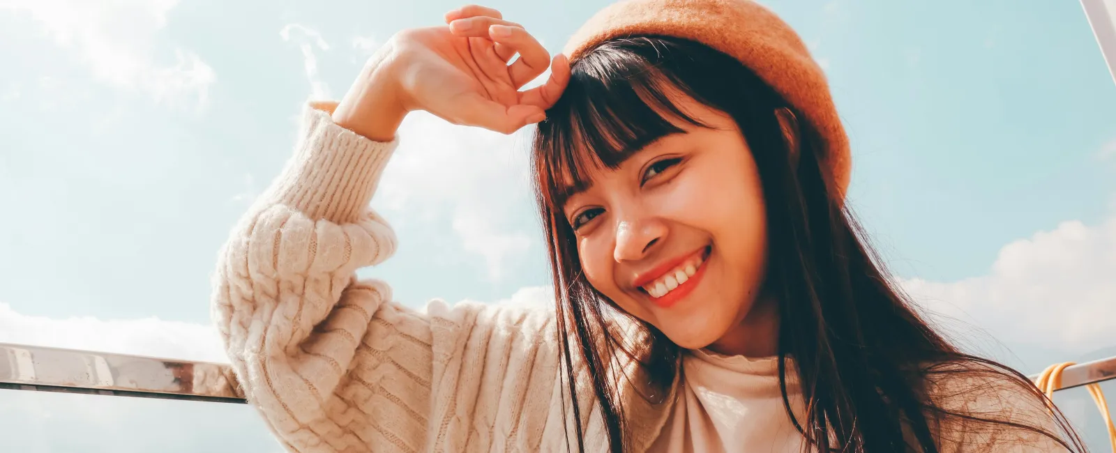 Smiling woman wearing a beret and cozy sweater against a bright sky backdrop.