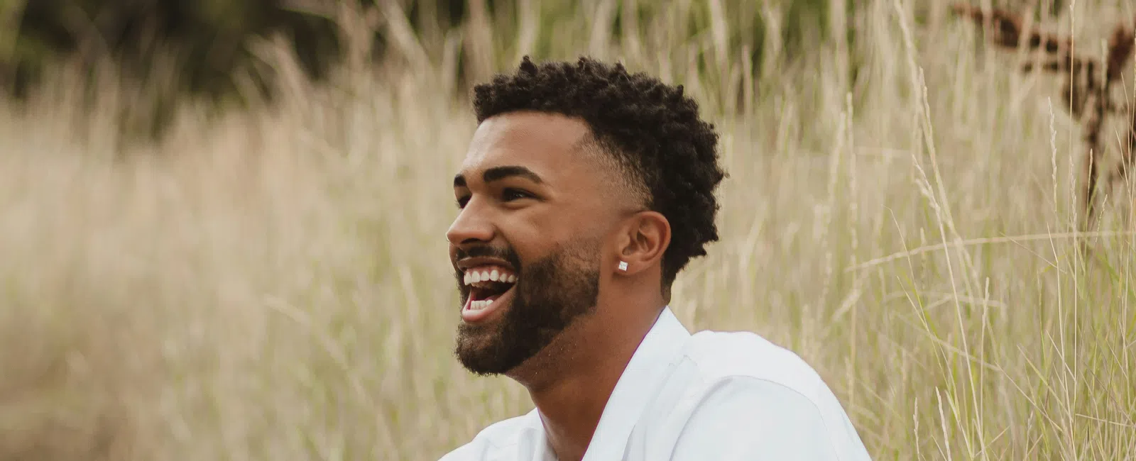 Smiling man in white shirt and shorts sitting on rock in a grassy outdoor setting enjoying nature.