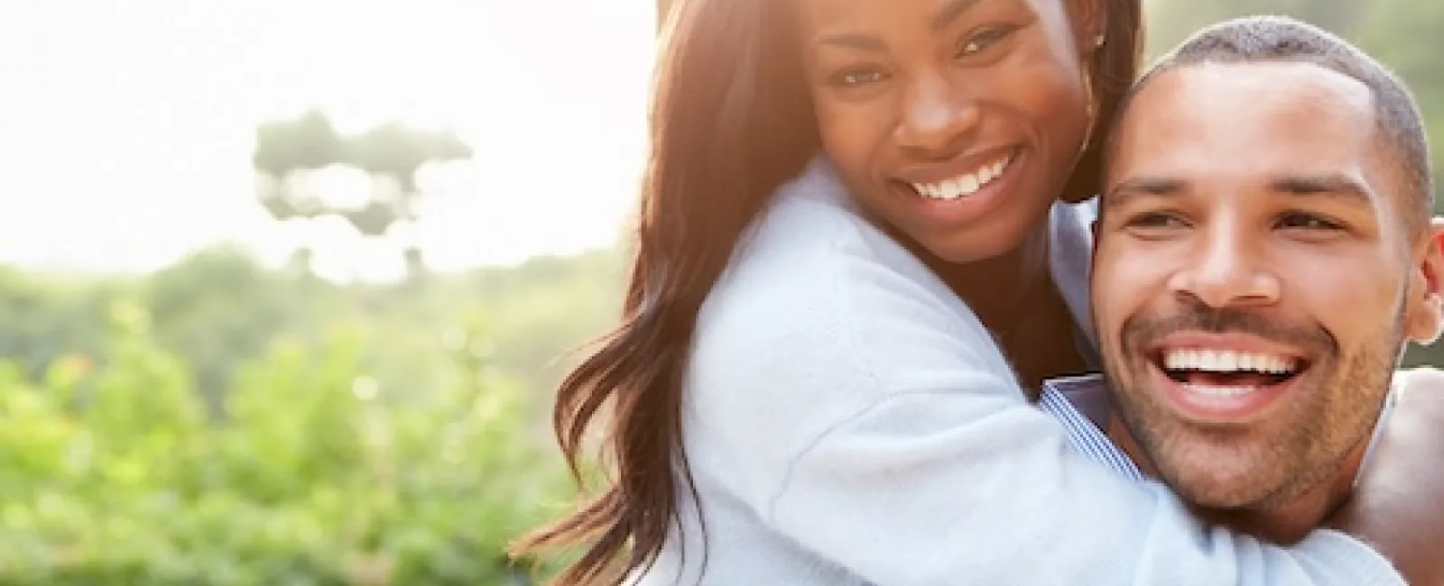 Happy young couple enjoying outdoors with woman hugging man from behind in a sunny green park