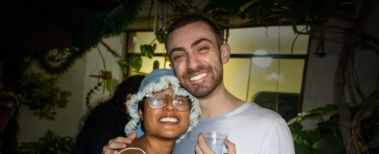 Happy couple smiling and hugging at an outdoor evening party surrounded by plants and lights