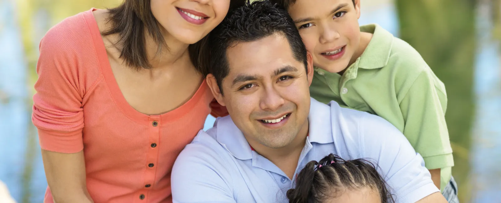 Smiling family of four sitting outdoors by a pond on a sunny day enjoying quality time together.