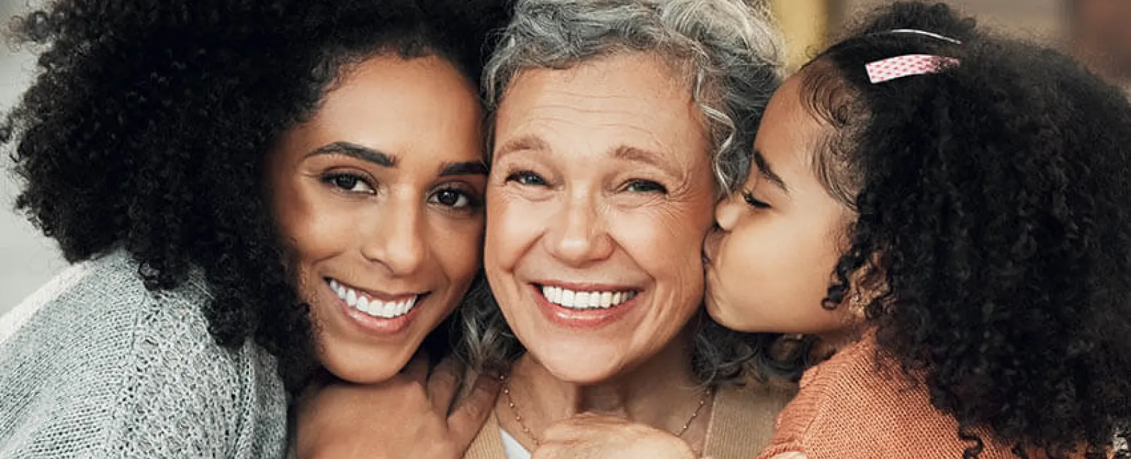 Three generations of women smiling together, showcasing love and family bonds in a cozy indoor setting.