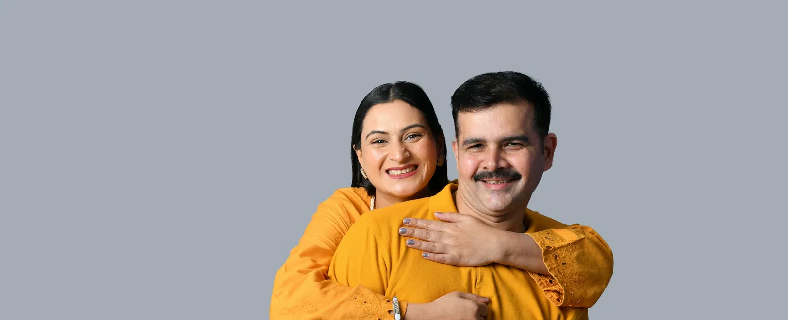 Happy couple wearing matching orange outfits smiling and hugging against a plain gray background