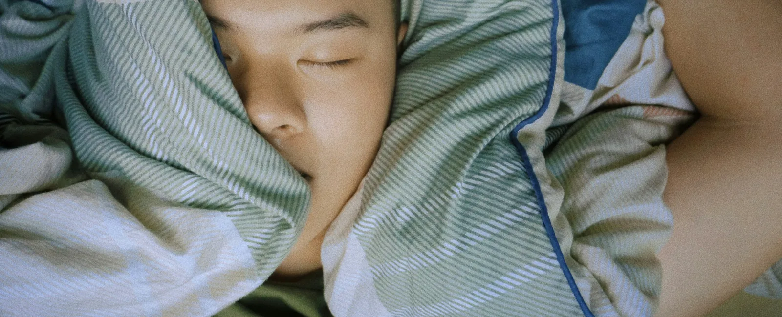 Person sleeping peacefully under green and white striped blanket with arm resting beside head