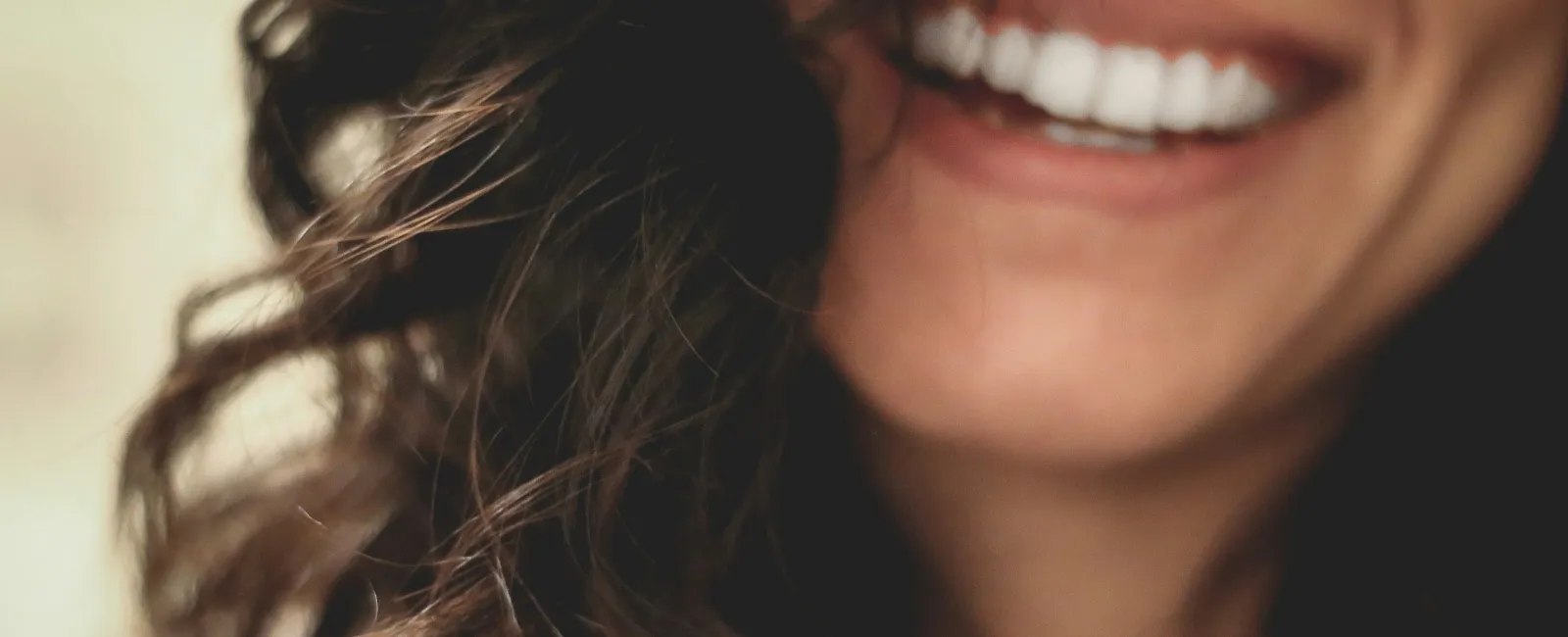 Close-up of a smiling woman with curly dark hair showing white teeth and joyful expression.