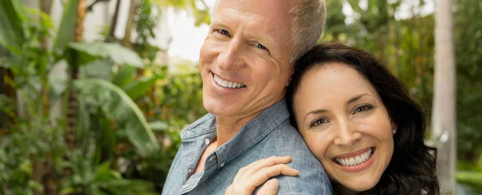 Happy mature couple embracing outdoors in a lush green garden with smiles, showing affection and warmth.