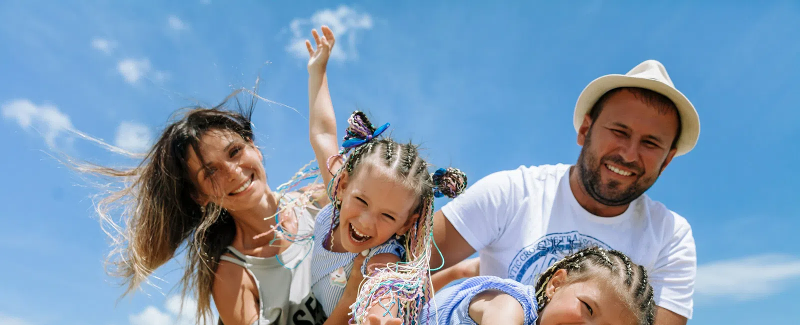 Happy family of four playing and smiling on a sunny beach with blue sky and ocean in the background