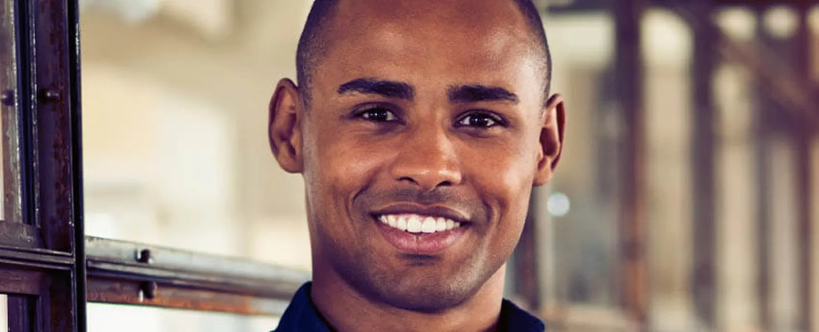 Smiling man in a navy shirt standing confidently with arms crossed in an industrial setting.