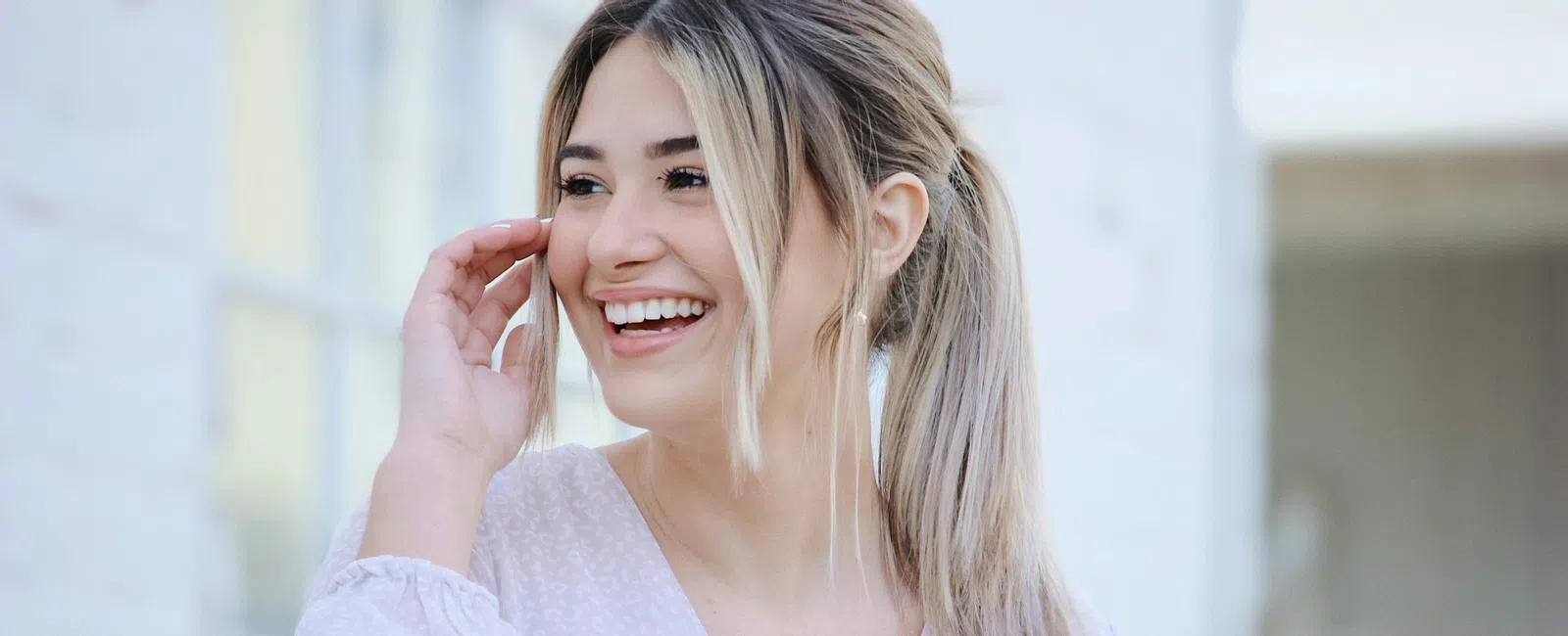 Smiling young woman with blonde hair in a ponytail wearing a light pink blouse outdoors