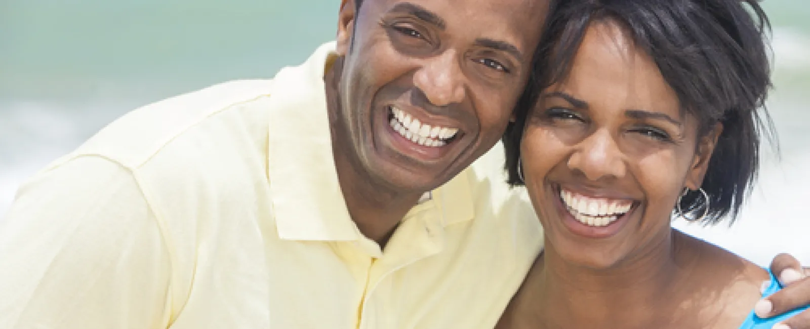 Happy smiling African American couple posing together at the beach with ocean in the background.