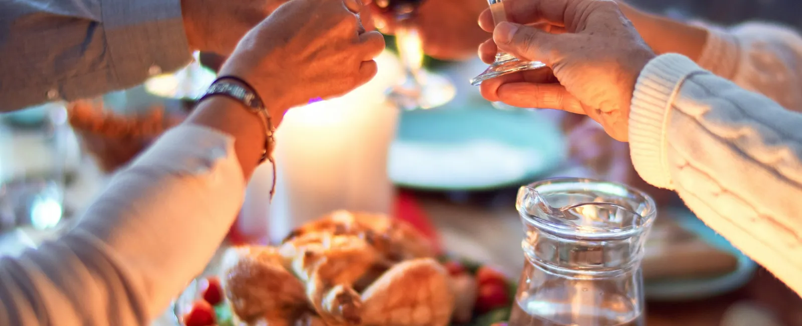 Friends clinking wine glasses over a festive dinner table with roasted chicken and lit candles.