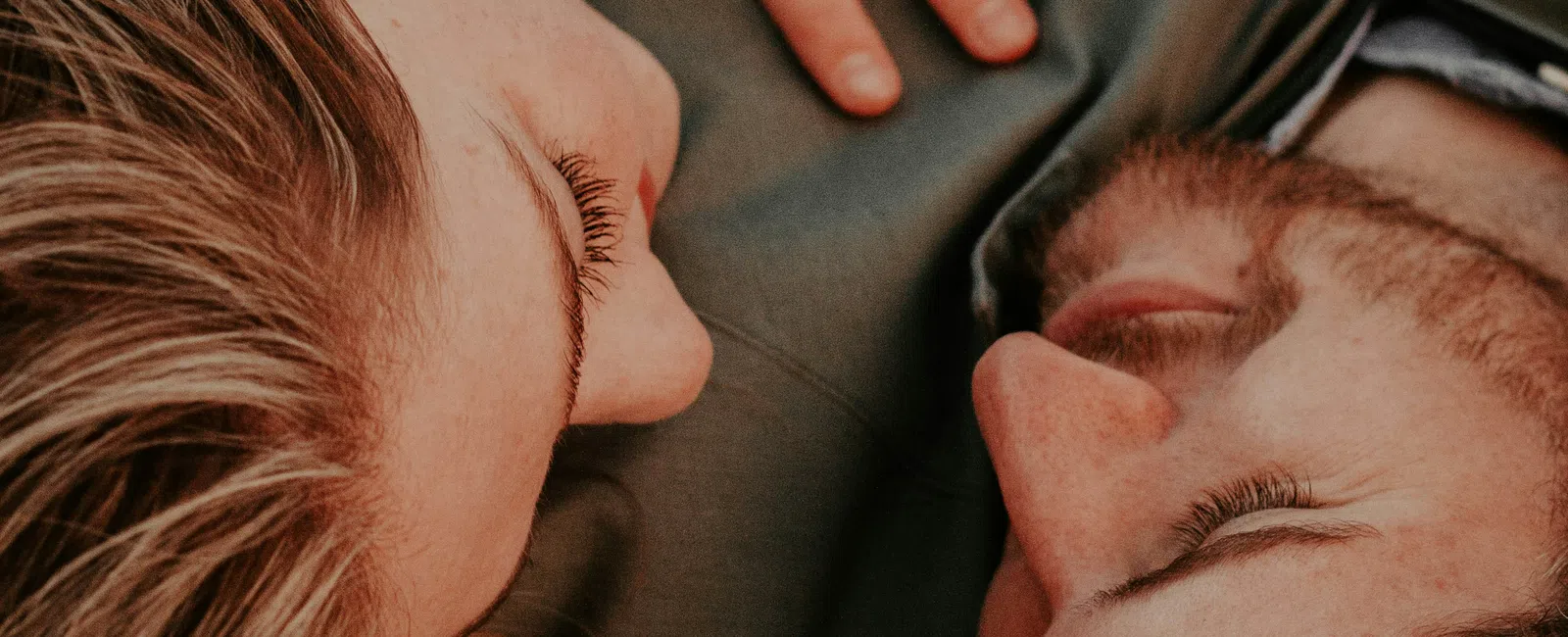 Couple lying close with eyes closed, woman's hand with ring resting on man's chest, intimate moment.
