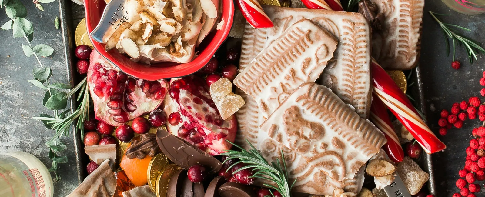 Festive tray with assorted holiday treats including gingerbread, candy canes, pomegranate, chocolate, and fresh fruit.