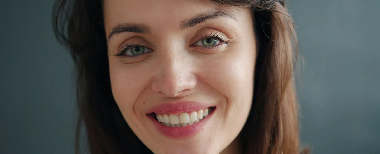 Close-up portrait of a smiling young woman with green eyes and brown hair against a gray background