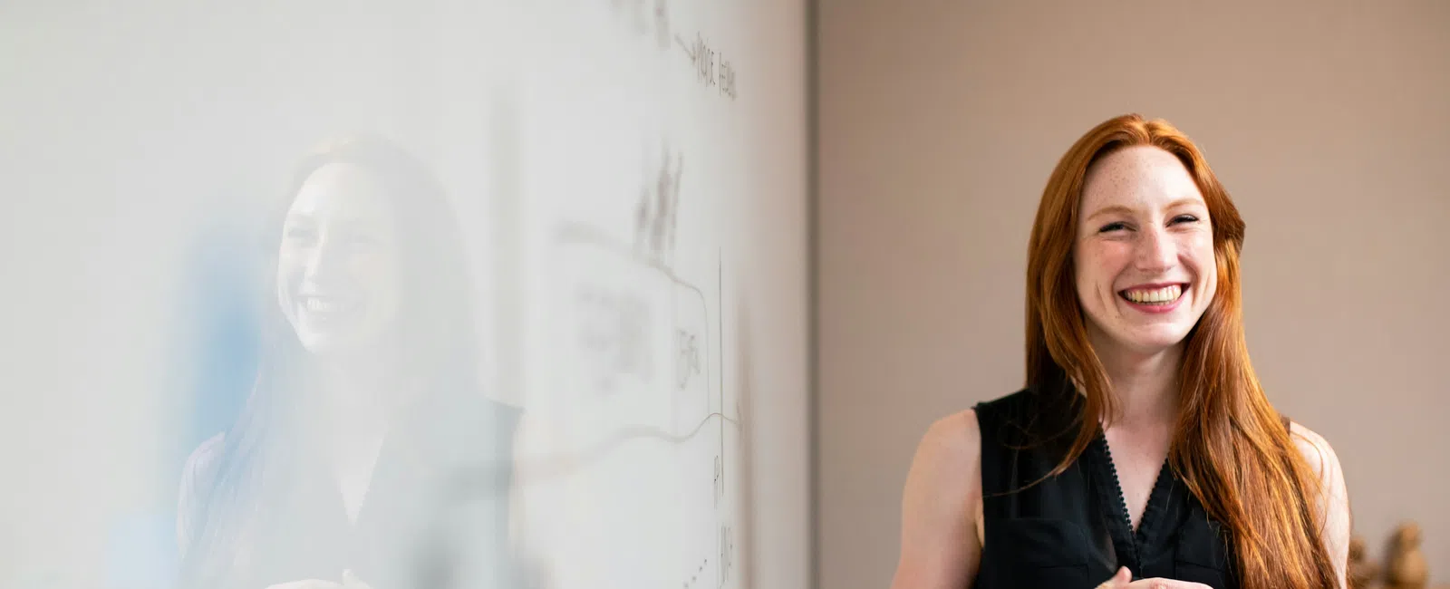 Smiling red-haired woman standing in front of a whiteboard in a modern office setting