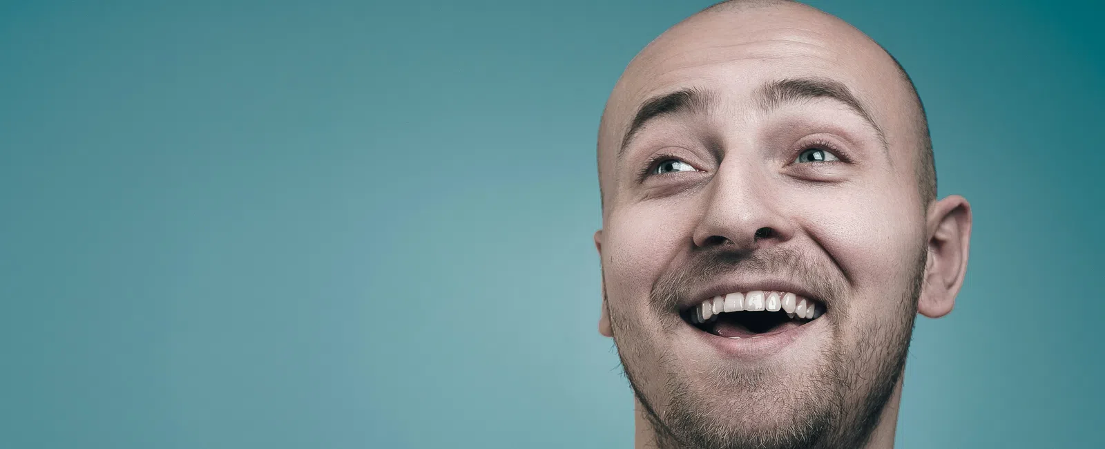 Smiling bald man with a beard wearing a white t-shirt against a blue background.