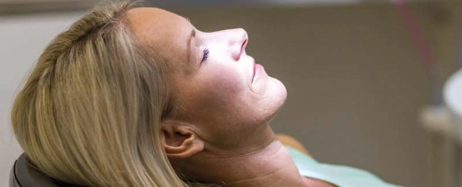 Woman relaxing in dental chair with light shining on her face during a dental appointment.