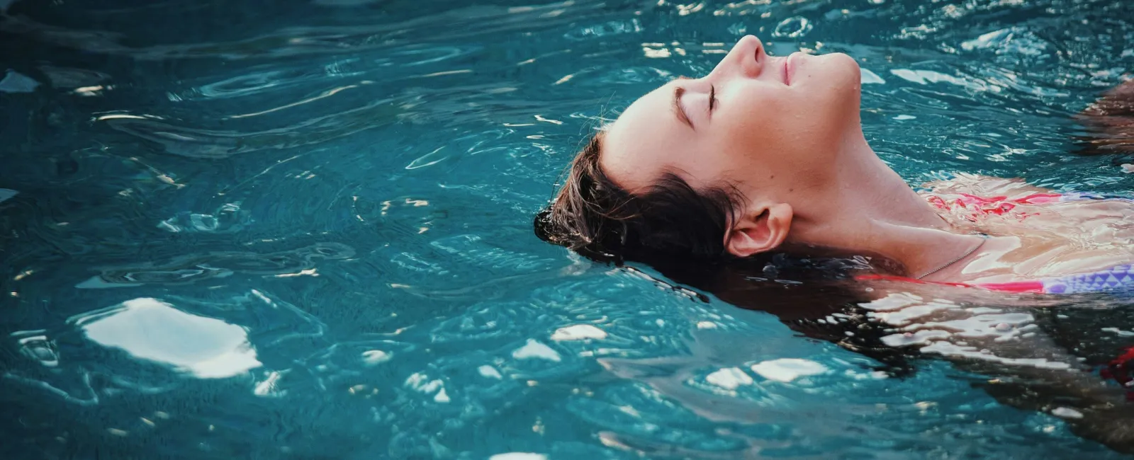 Woman relaxing and floating peacefully on her back in a clear blue swimming pool.