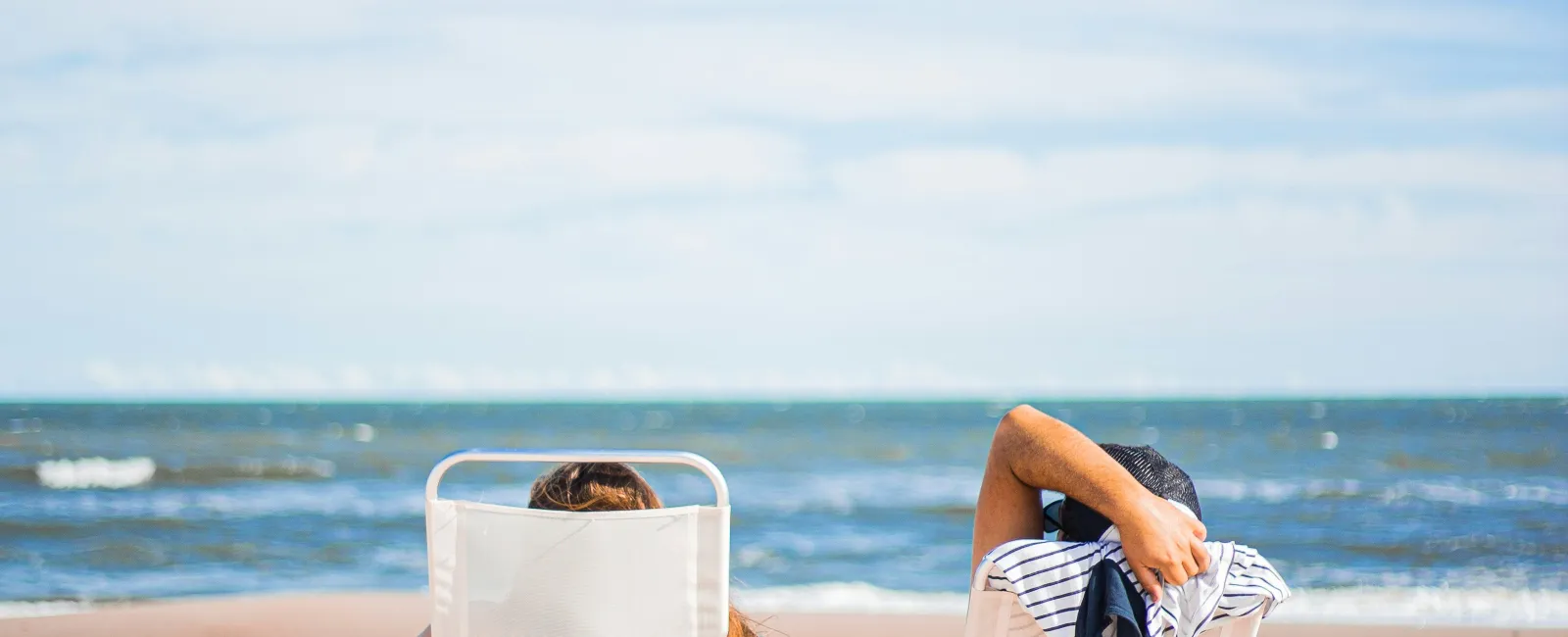 Couple relaxing on beach chairs facing the ocean under a clear blue sky on a sunny day