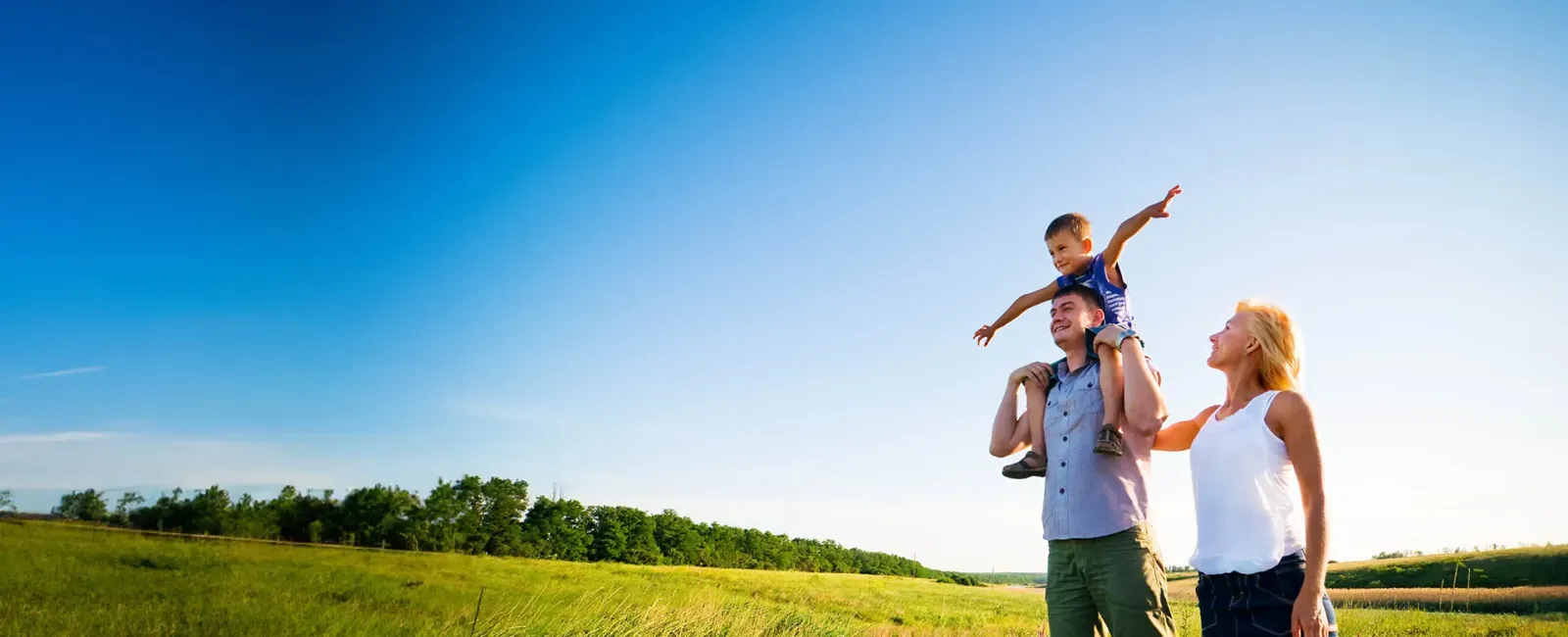 A happy family with a child on the father's shoulders, enjoying a sunny day in a meadow.