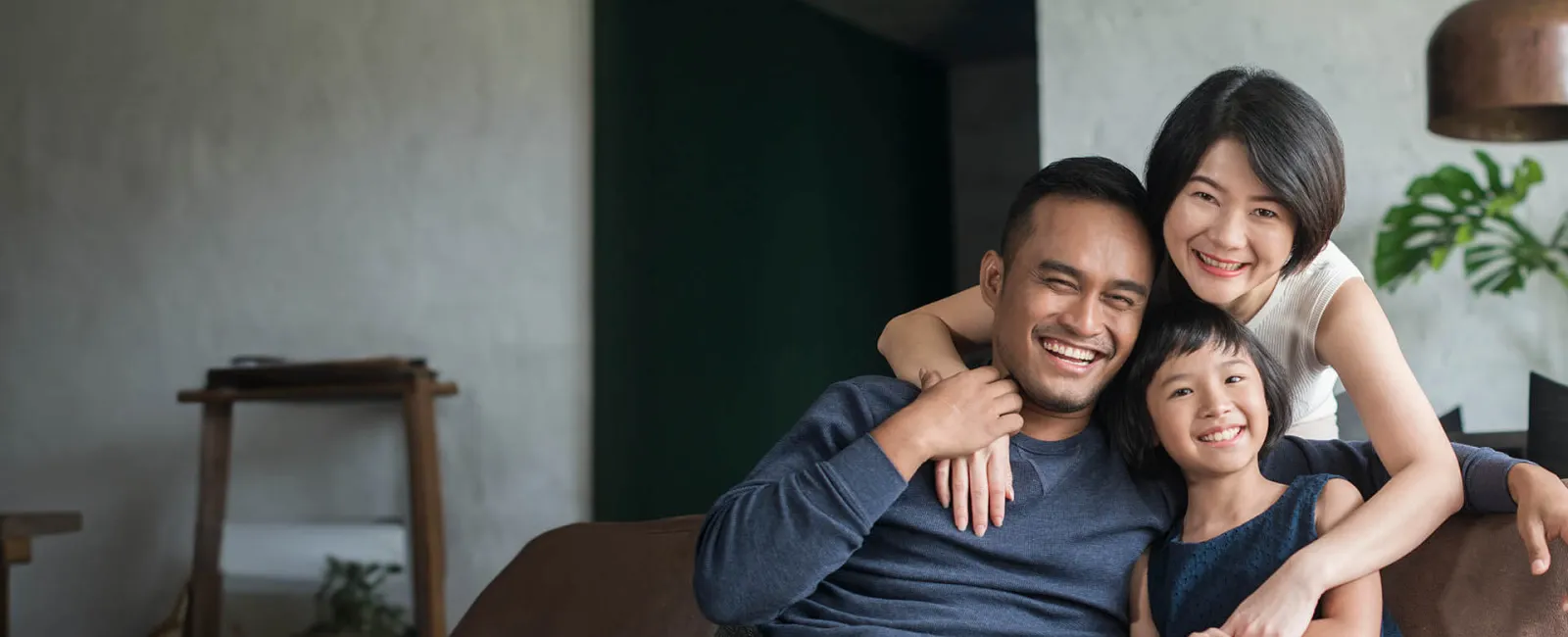 Happy family portrait with parents and child smiling together in a cozy living room setting.
