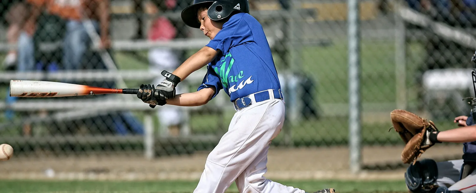 Young baseball player in blue batting during a game with catcher and ball in view on a sunny day.