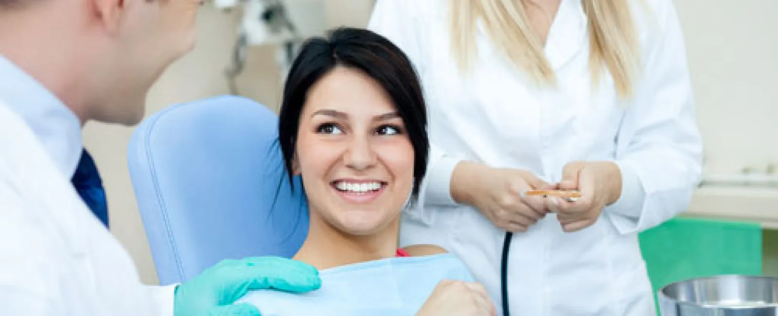 Smiling woman patient in dental chair with dentist and dental assistant in clinic setting