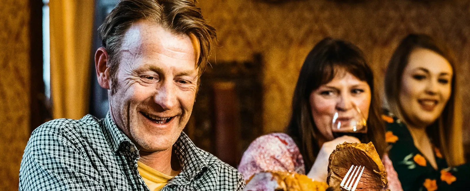 Group of people enjoying a meal with carved roast beef and wine at a dinner table in a warm setting