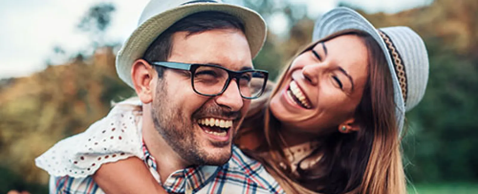 Happy young couple wearing hats laughing outdoors in a park on a sunny day