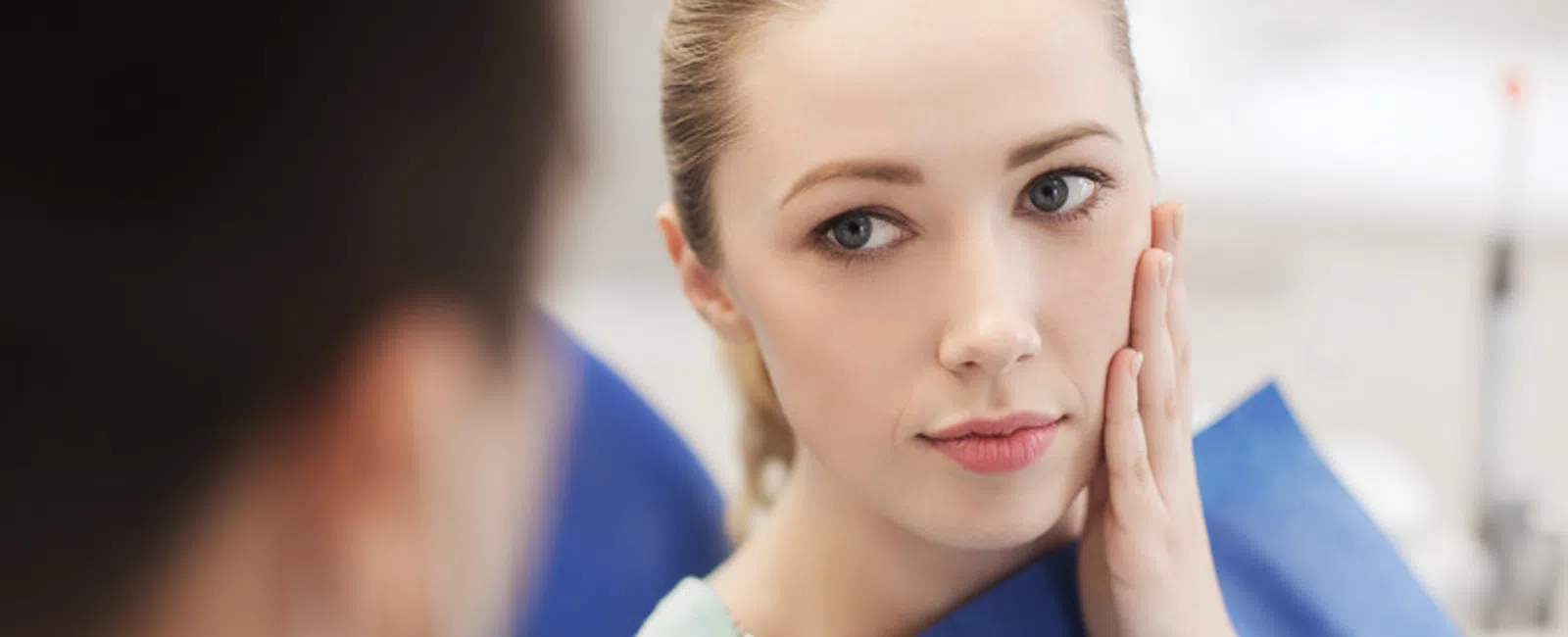 Young woman at dentist appointment holding her cheek, concerned about dental pain or examination.