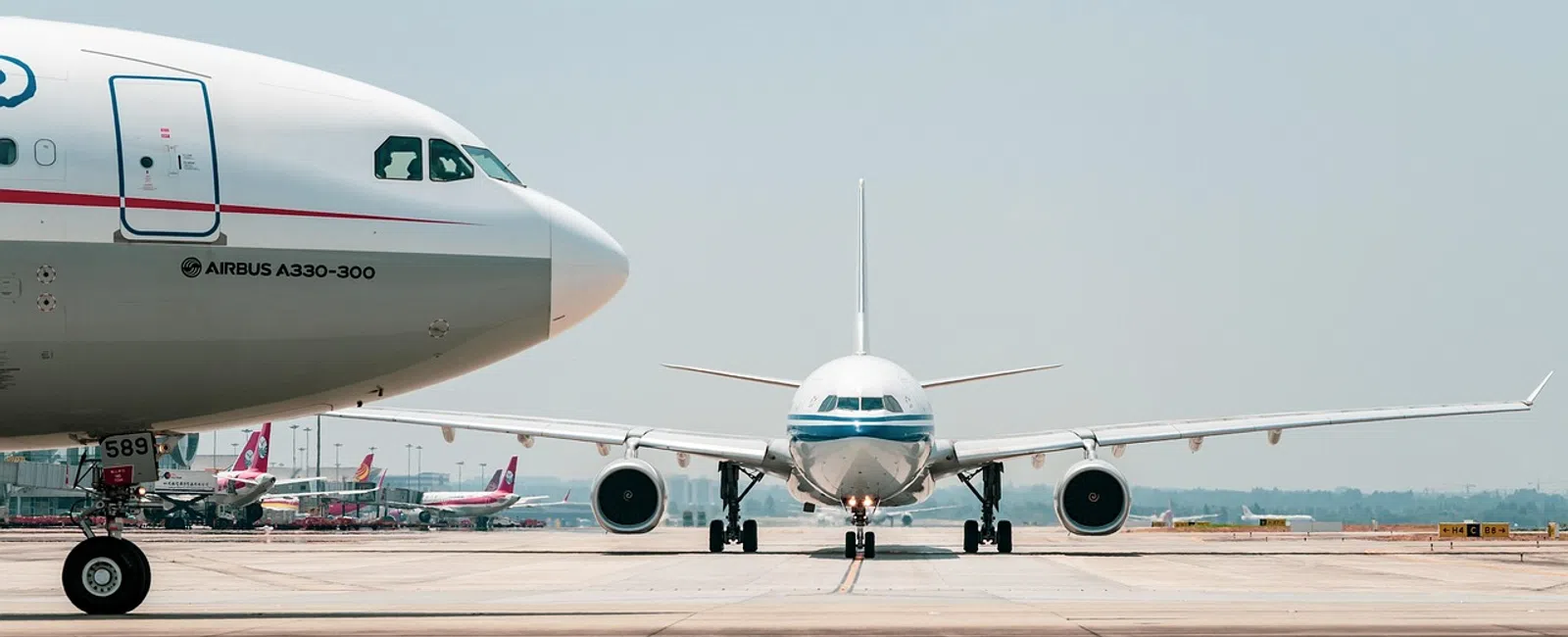 Two commercial airplanes on a runway, one facing forward and the other showing side view with clear sky above.