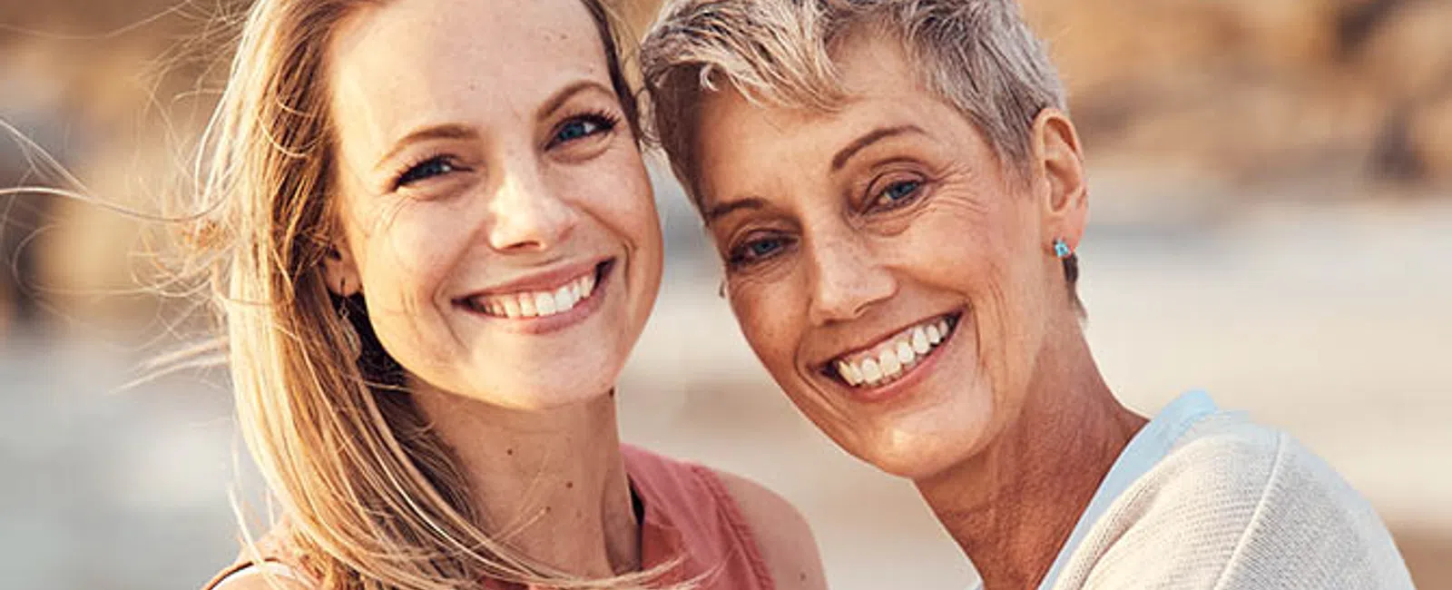 Two women smiling and hugging outdoors in warm natural light with a blurred background