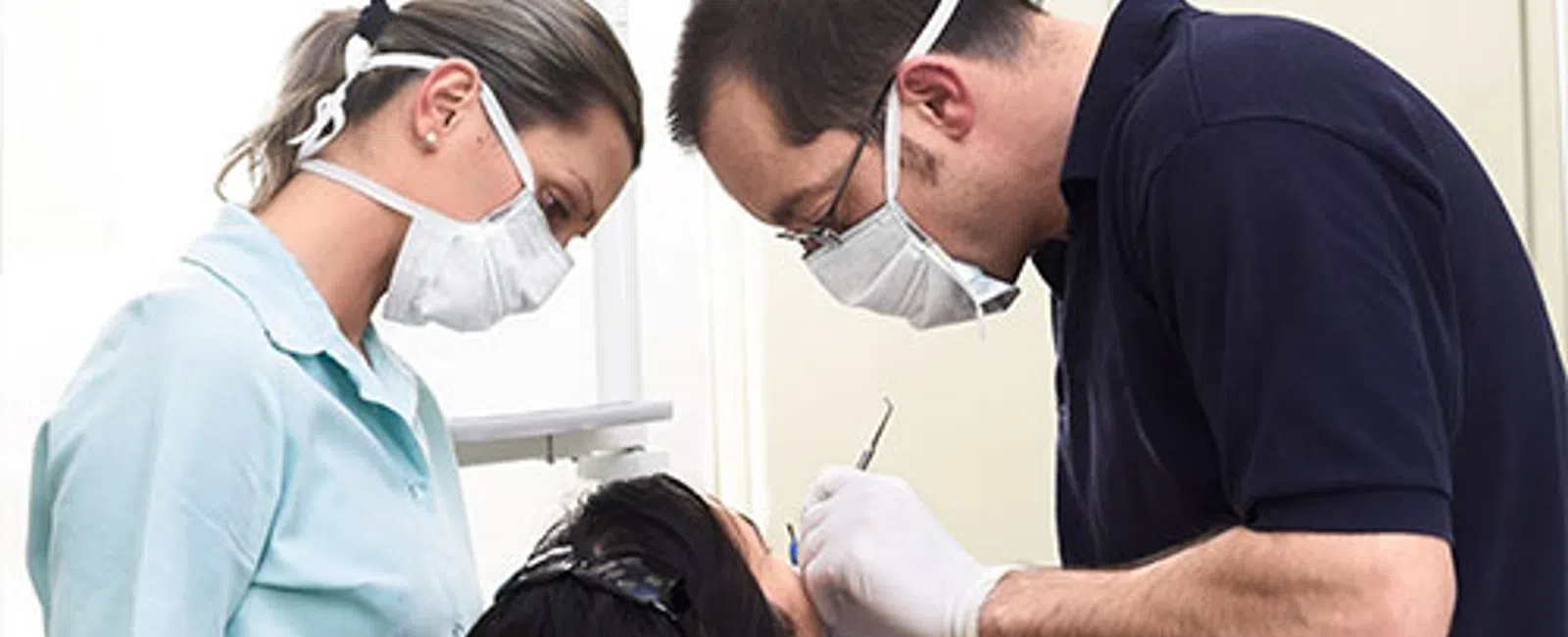 Dentist and assistant wearing masks examining patient in dental clinic during treatment.