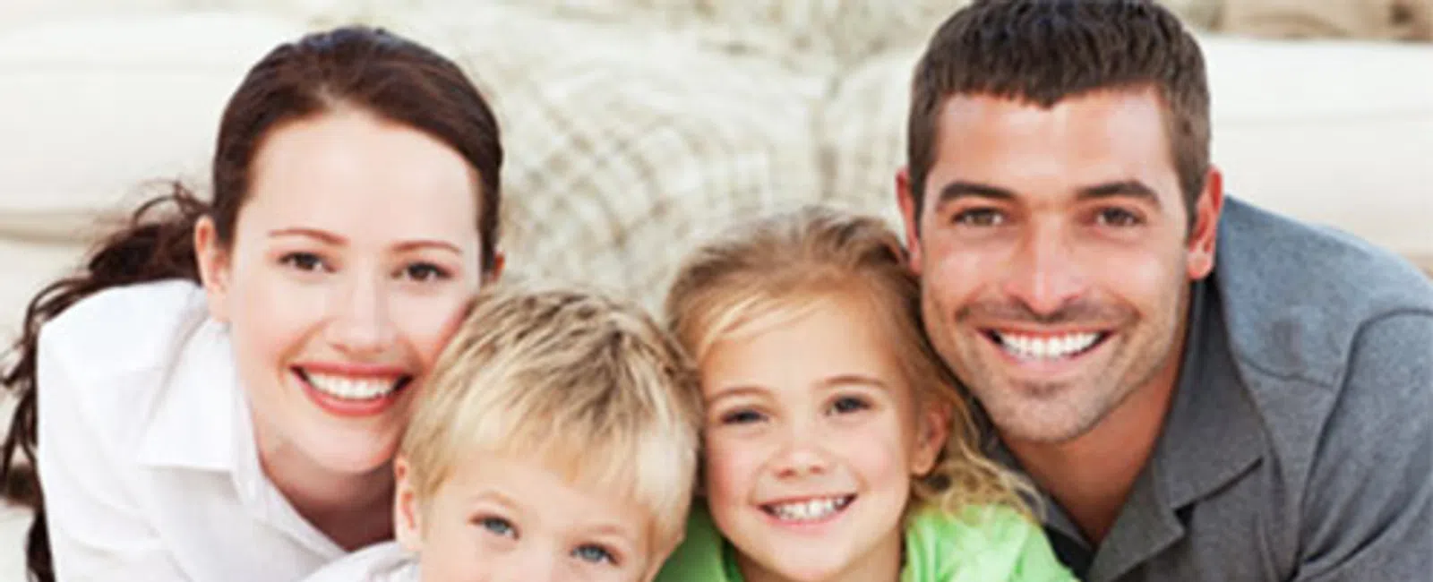 Happy family of four with parents and children smiling and lying on a carpet indoors.