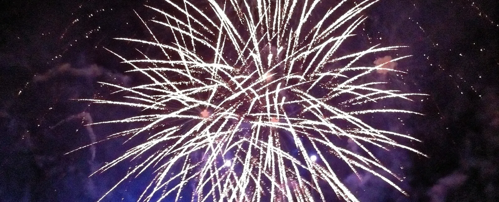 Bright white fireworks exploding in the night sky with purple smoke and dark background