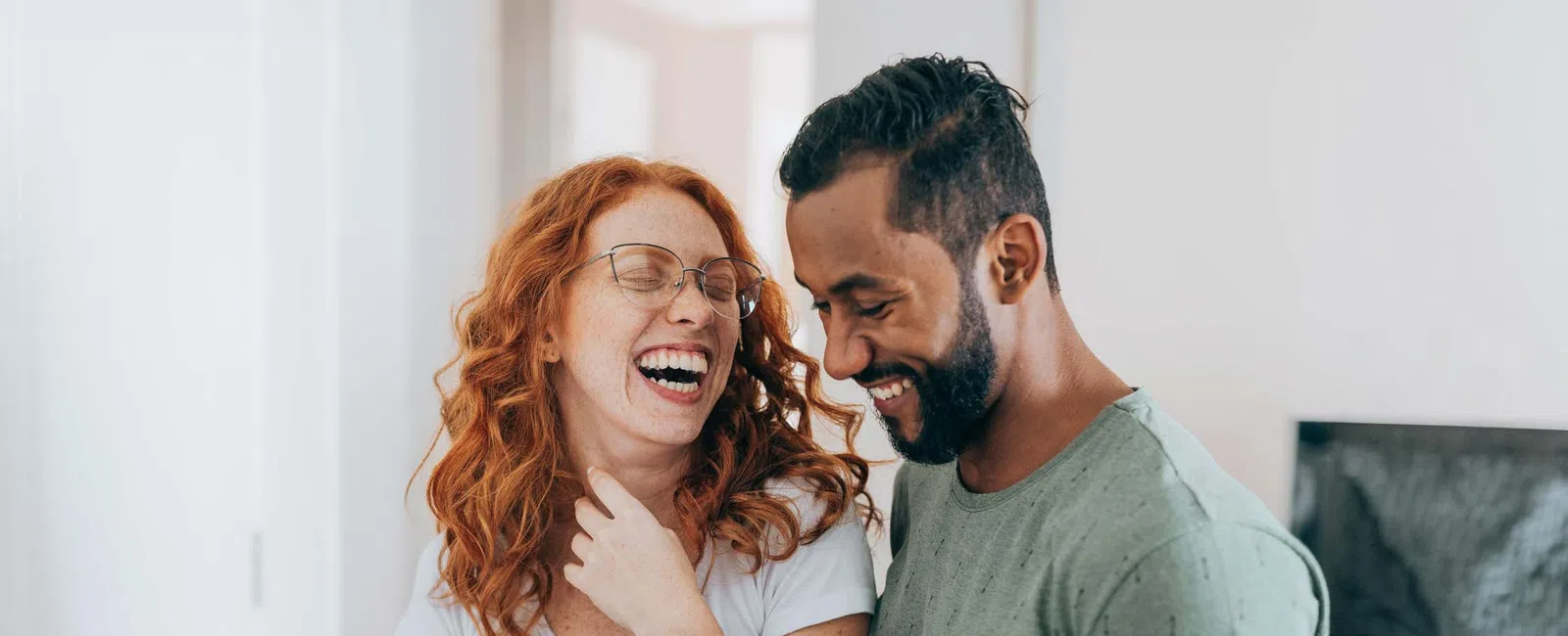 Couple laughing together while holding smartphones in a cozy modern living room setting