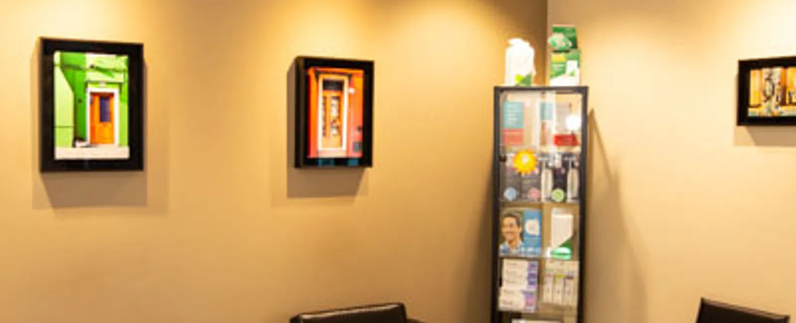Modern waiting room with black leather chairs, informational display cabinet, and colorful framed art on beige walls.