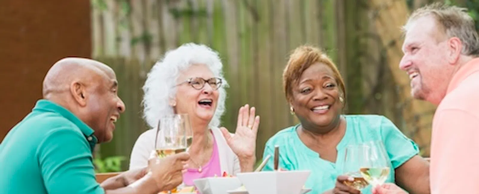 Diverse group of seniors enjoying outdoor meal and drinks together around wooden table.